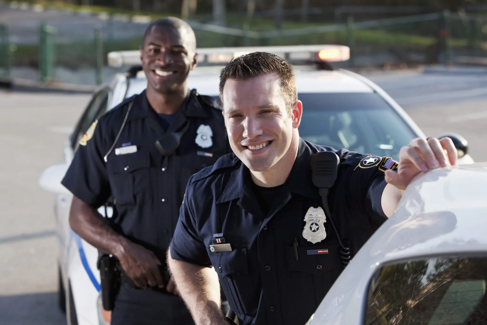 Two police officers, standing next to the police car and smiling | St. Louis Police Department is hiring a full-time police officer.