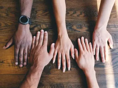 Four hands laying flat on a wooden table | New Member Groups